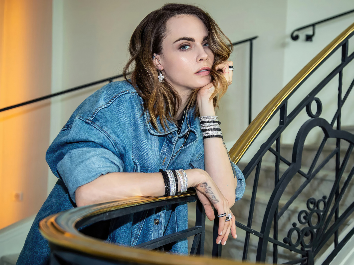 Актриса Кара Делевинь в джинсовой куртке стоит на лестнице