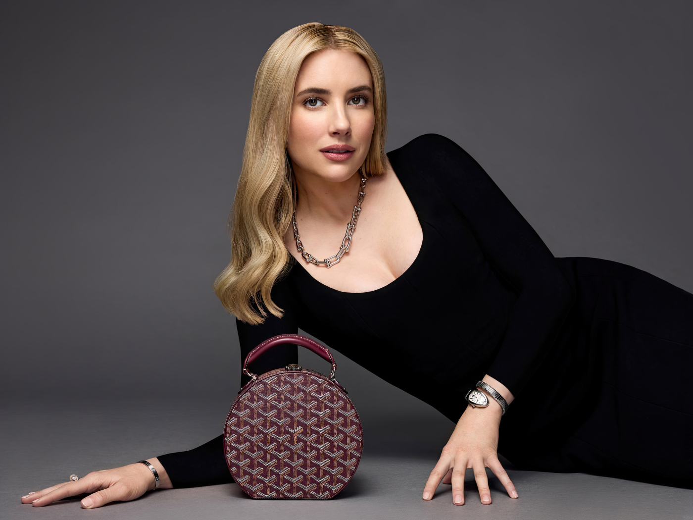 Актриса Эмма Робертс в черном платье с сумочкой лежит на сером фоне