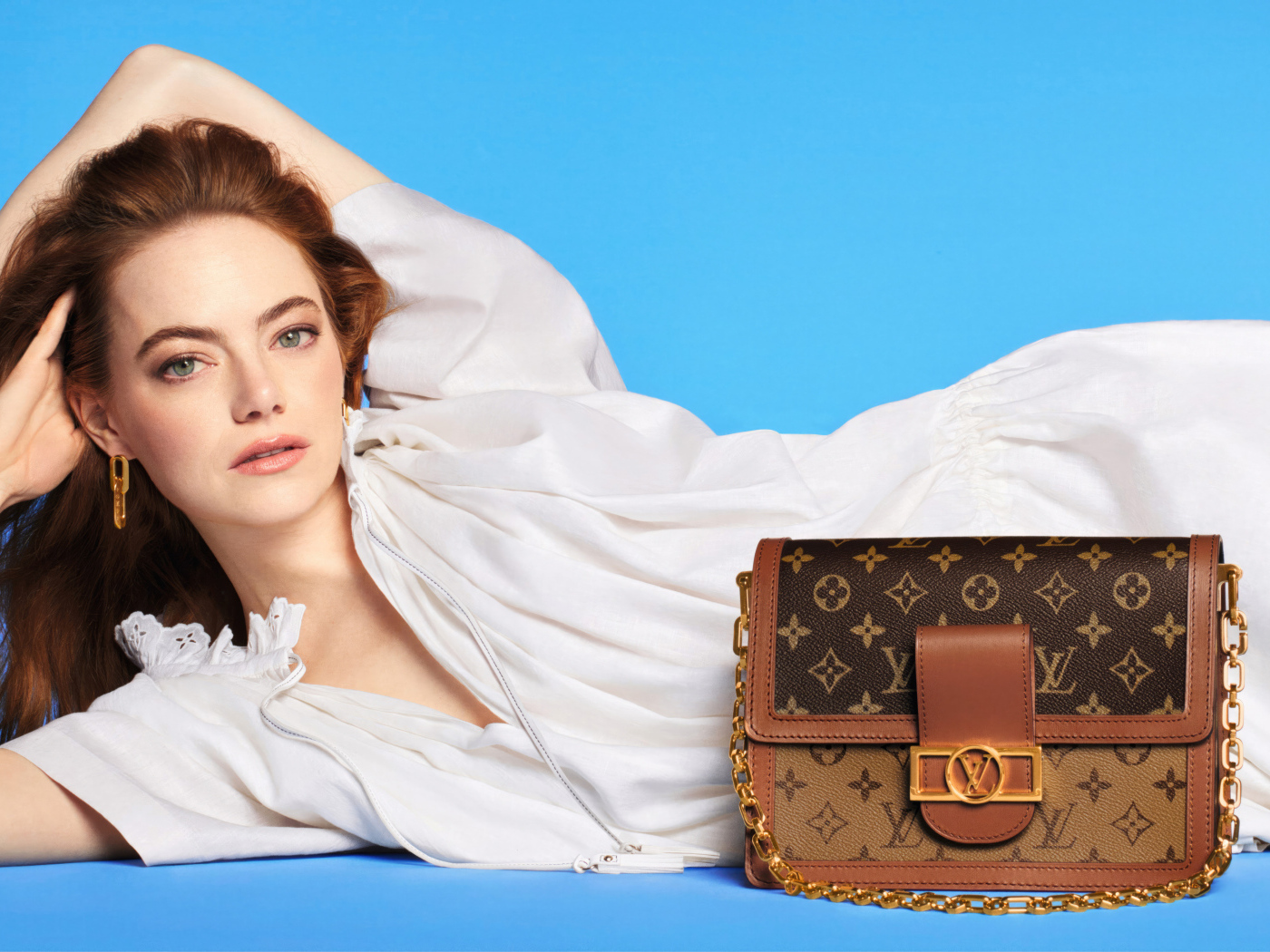 Актриса Эмма Стоун с сумочкой Louis Vuitton на голубом фоне