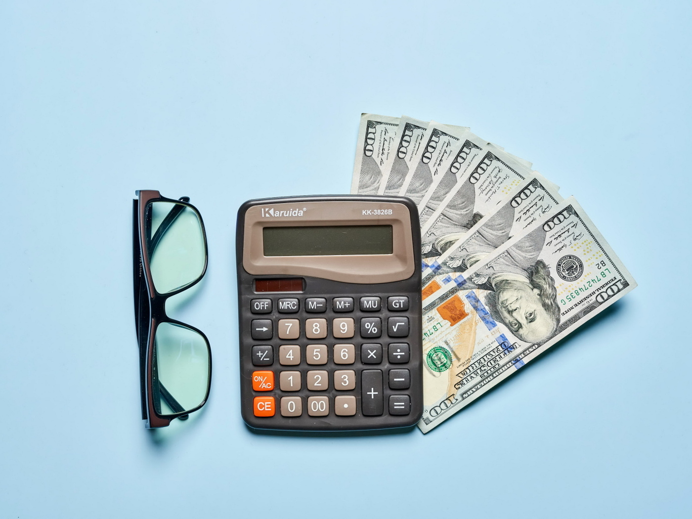 Очки, калькулятор и доллары на сером фоне