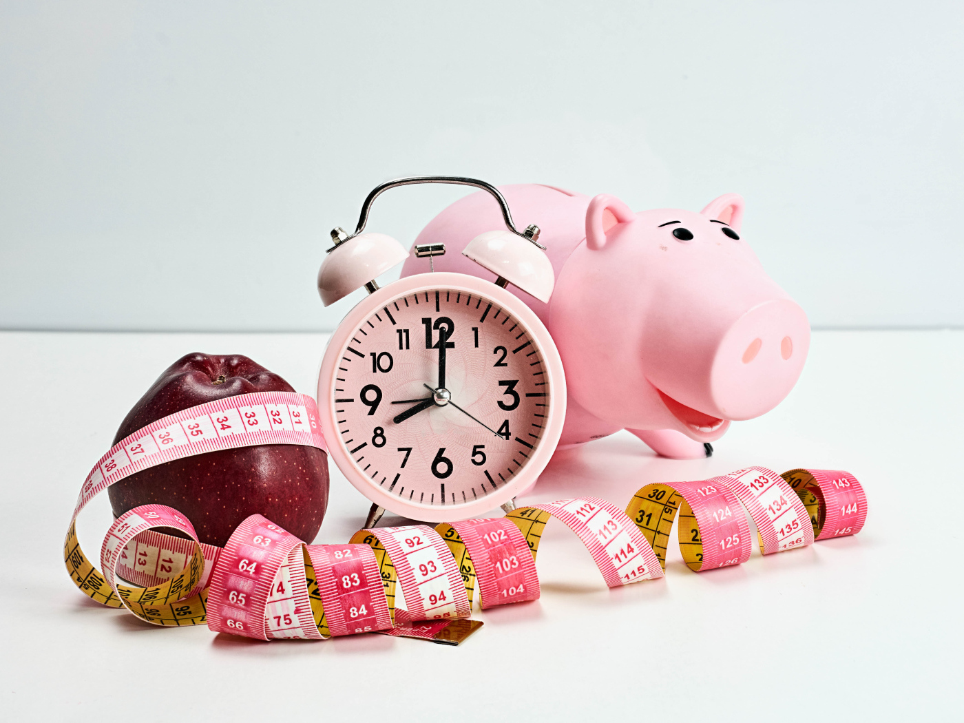 Мерная лента, яблоко, будильник и свинья копилка на белом фоне