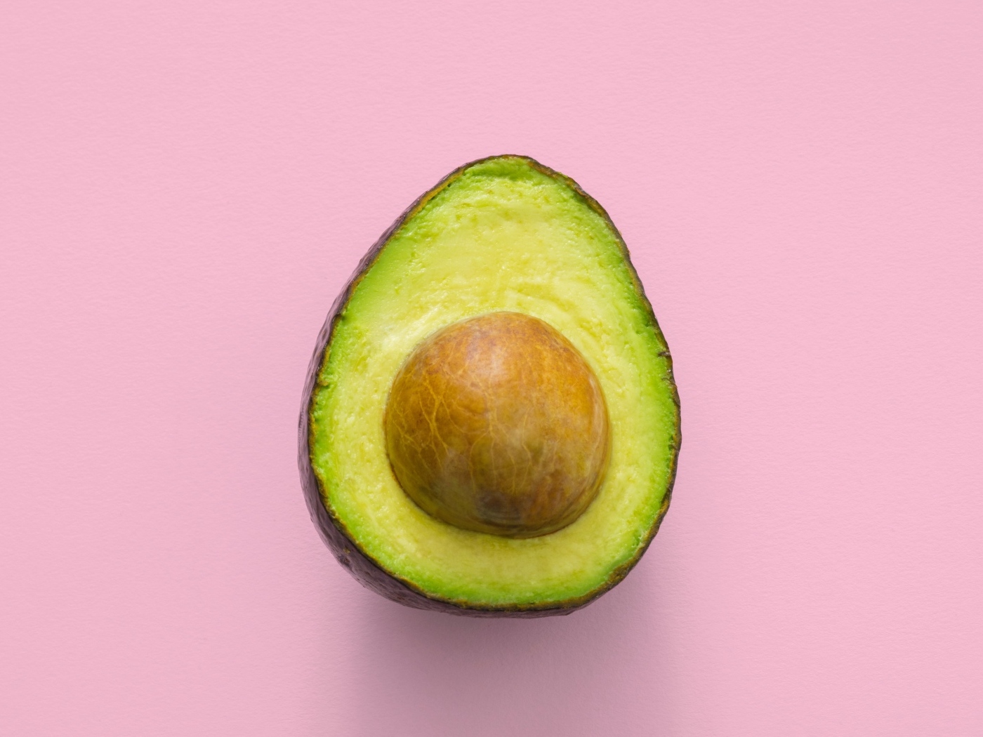 Половина авокадо с большой косточкой на розовом фоне