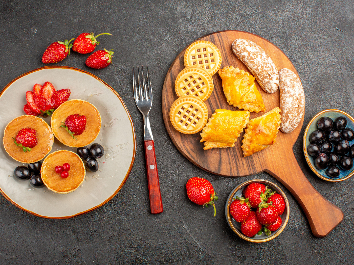 Печенье и оладьи на столе с ягодами клубники и виноградом