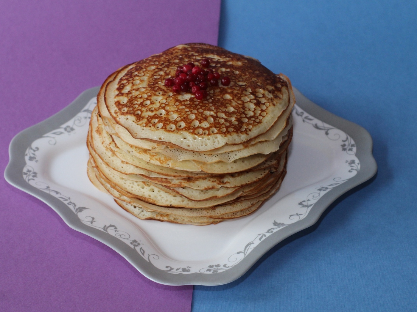 Тонкие блинчики с ягодами на большой тарелке на столе