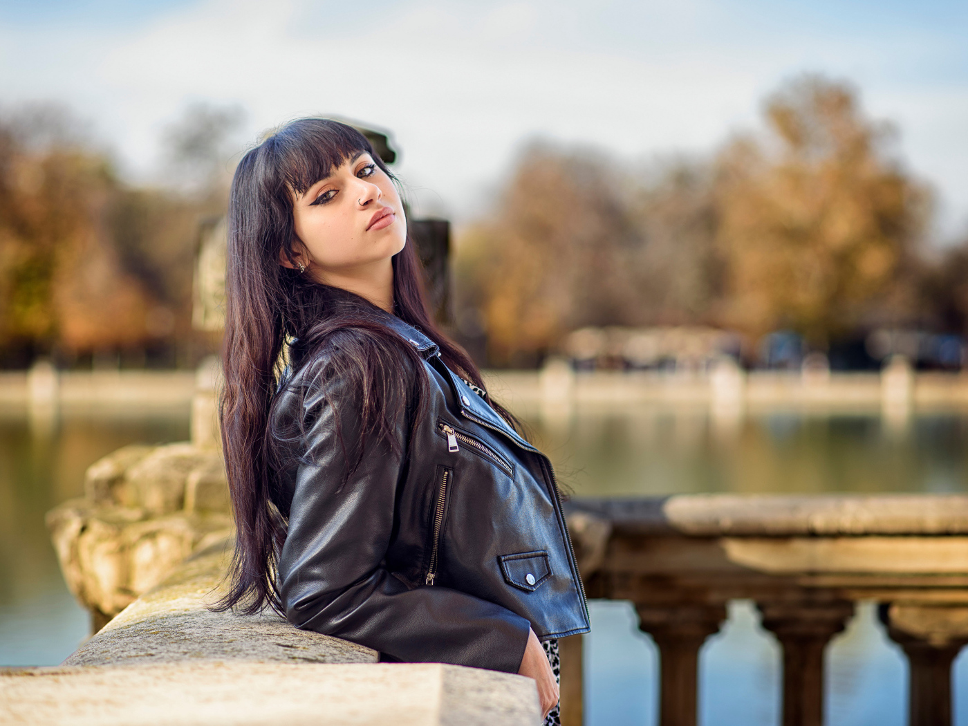 Девушка в черной куртке стоит на мосту у воды