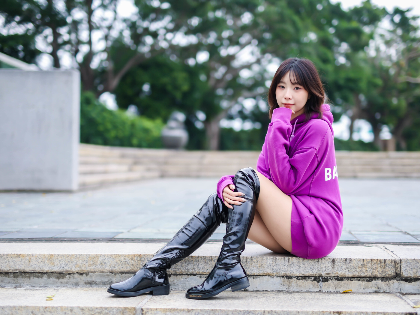 Девушка азиатка в длинных черных сапогах сидит на ступенях