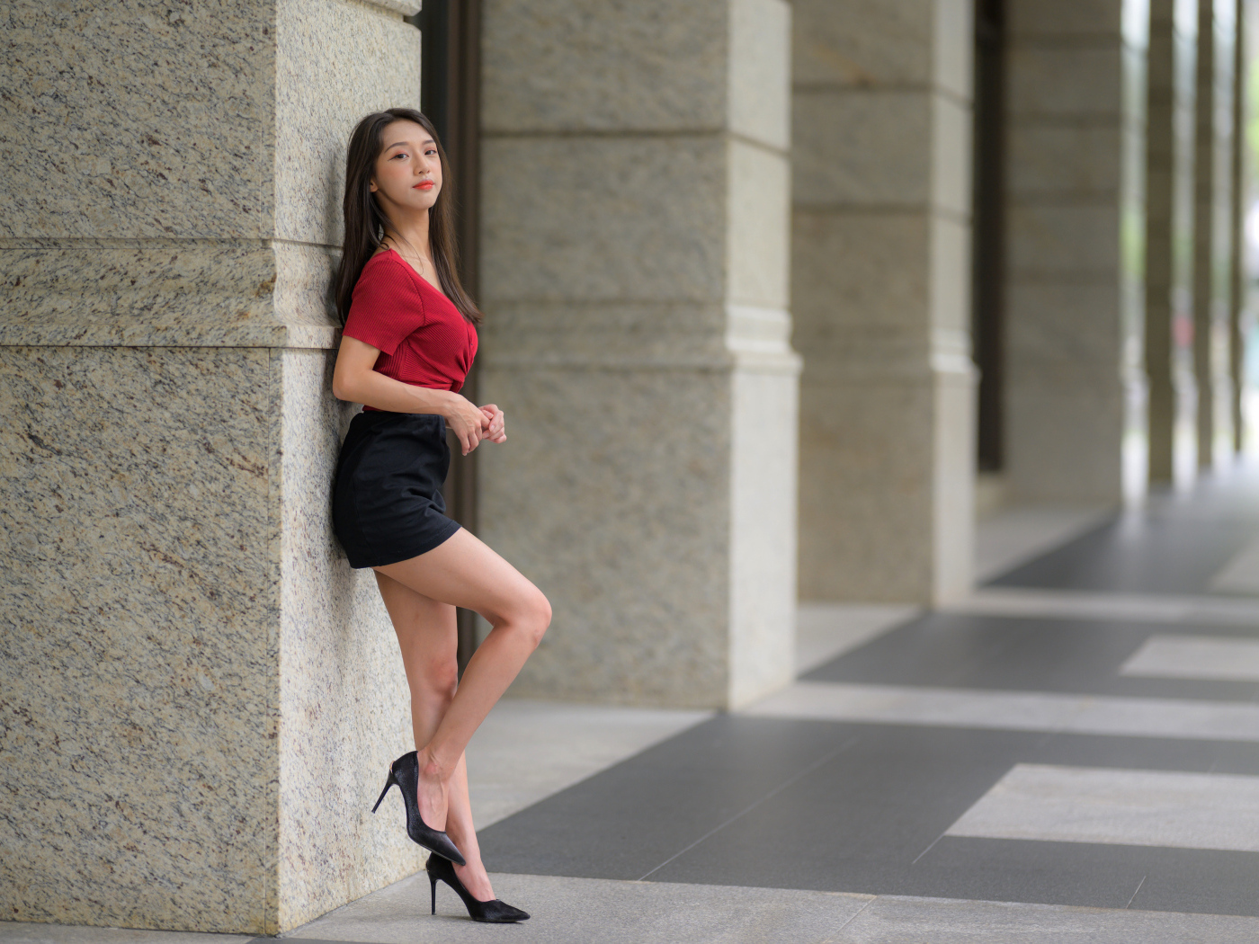 Азиатка в короткой черной юбке стоит у стены