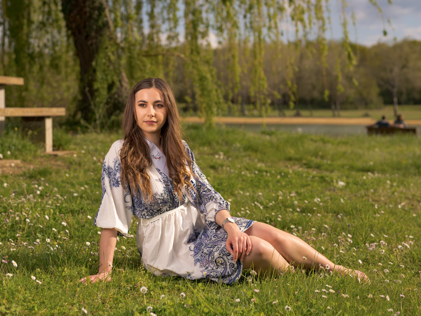 Красивая девушка в платье сидит на зеленой траве в парке