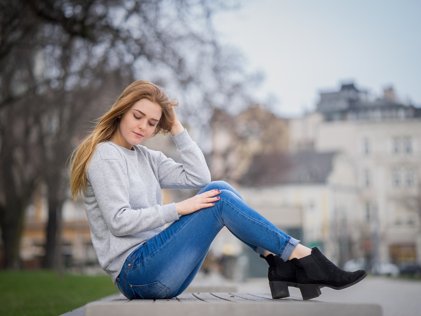 Милая девушка в синих джинсах сидит на лавке