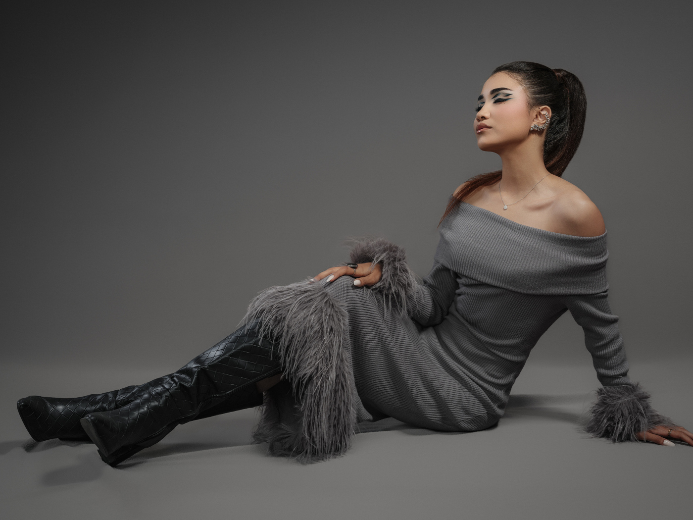 Девушка в платье и длинных черных сапогах на сером фоне