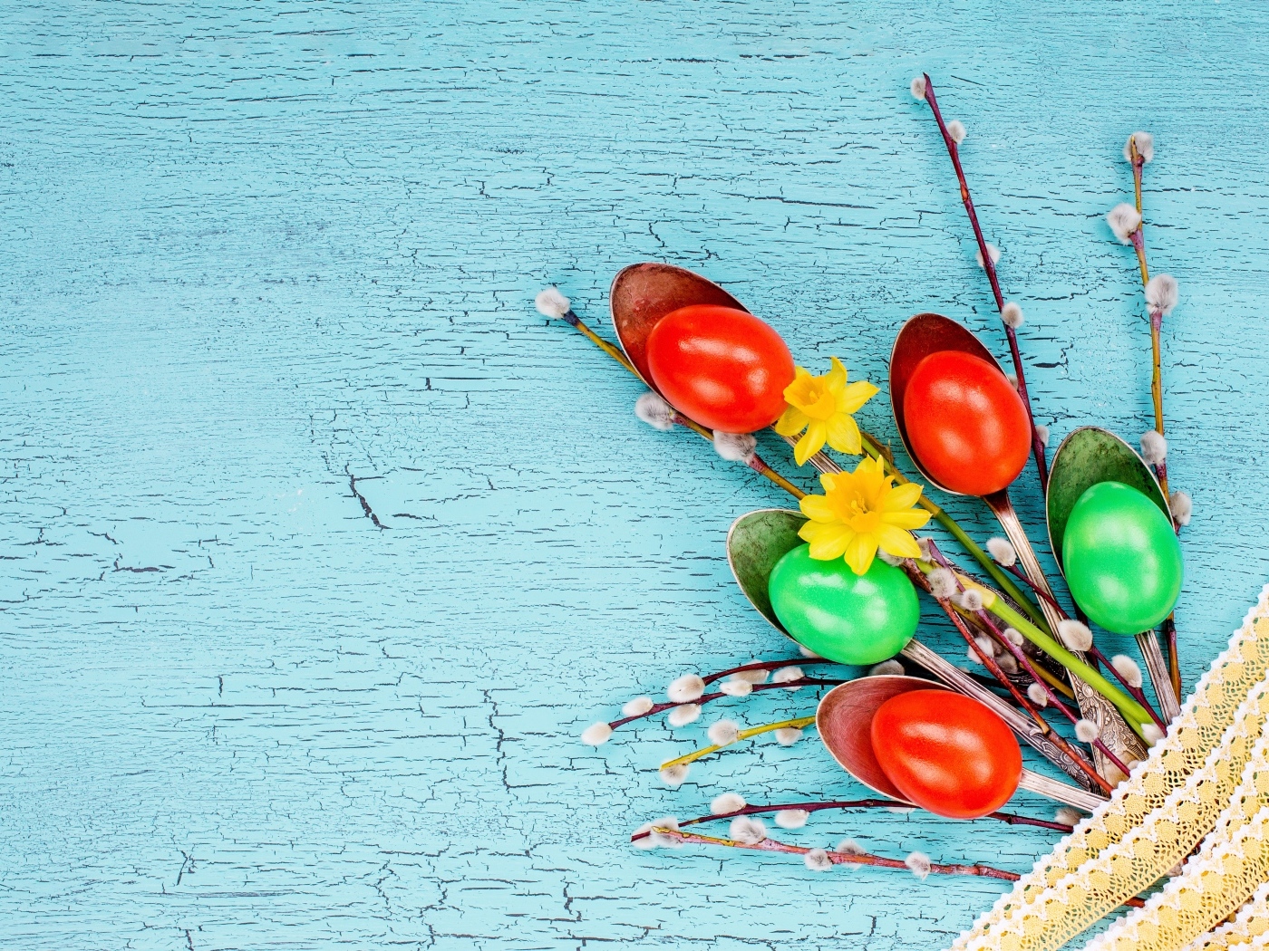 Ложки с разноцветными яйцами и ветками вербы на голубом фоне на Пасху