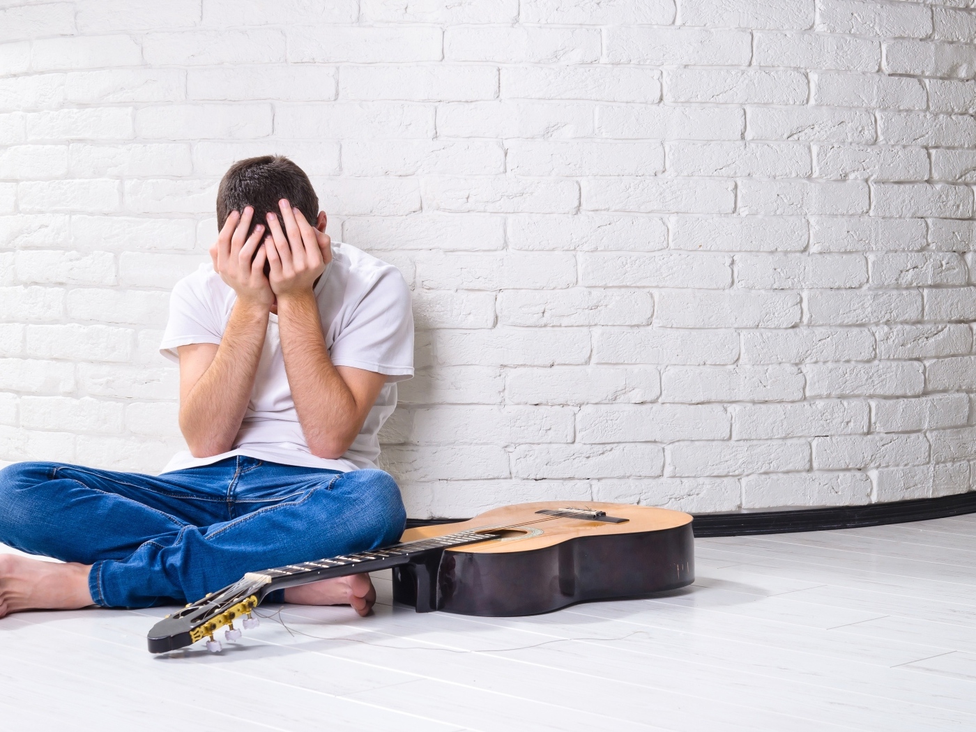 Мужчина с гитарой закрыл лицо руками у стены