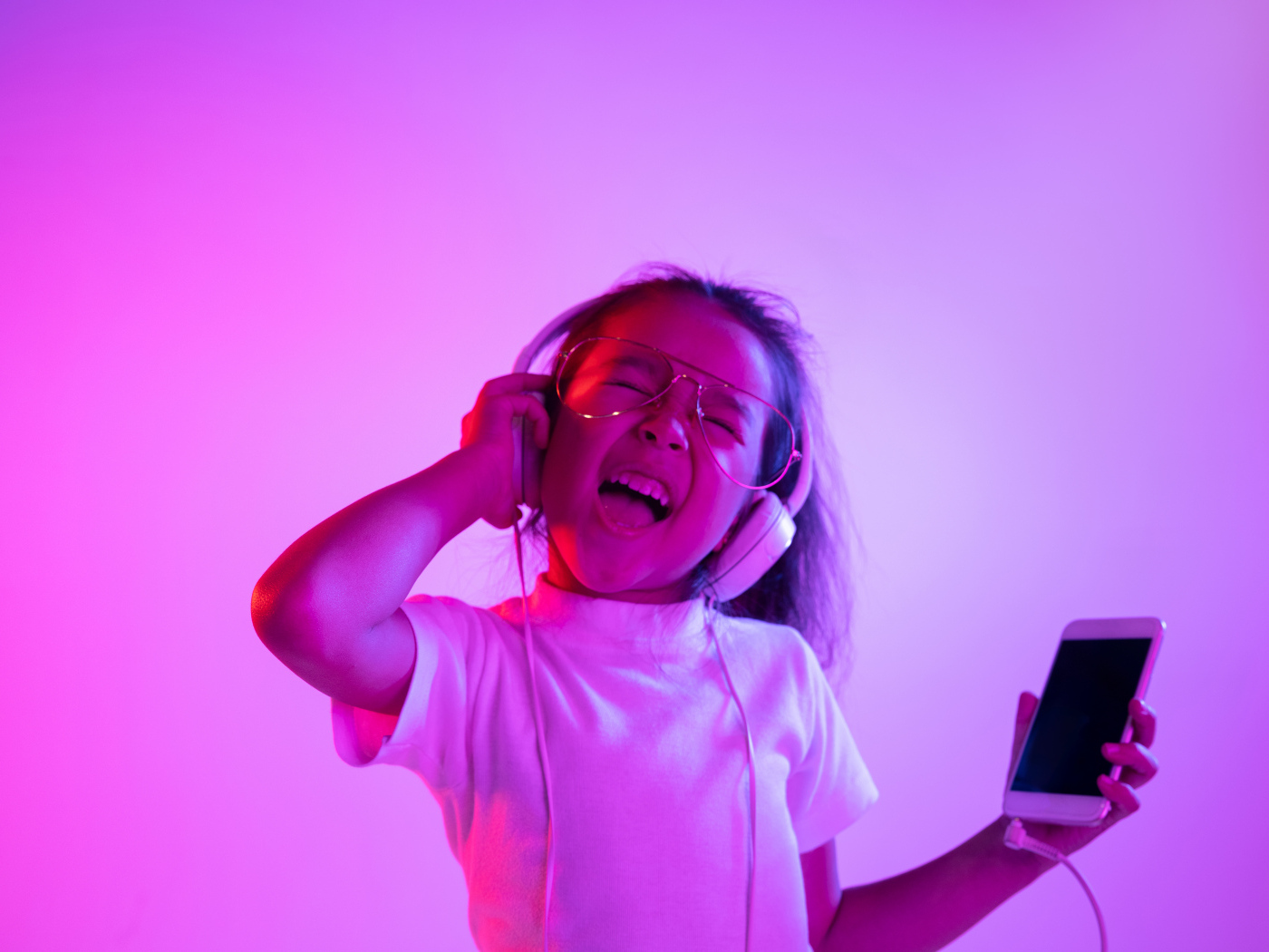 Маленькая девочка в наушниках с телефоном слушает музыку