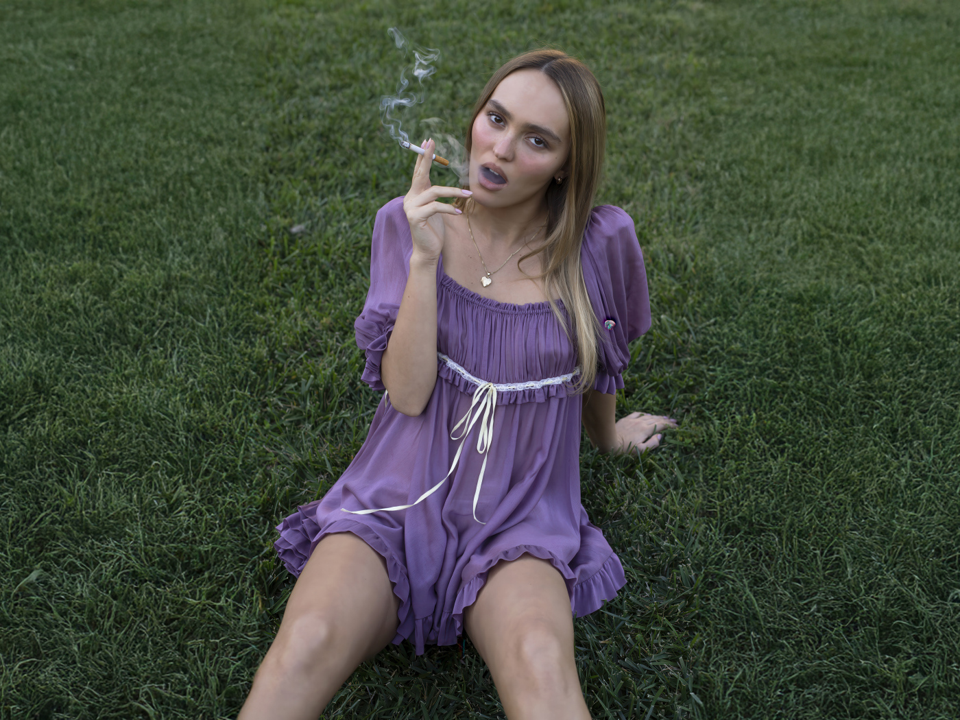 Молодая Лили-Роуз Депп с сигаретой сидит на траве