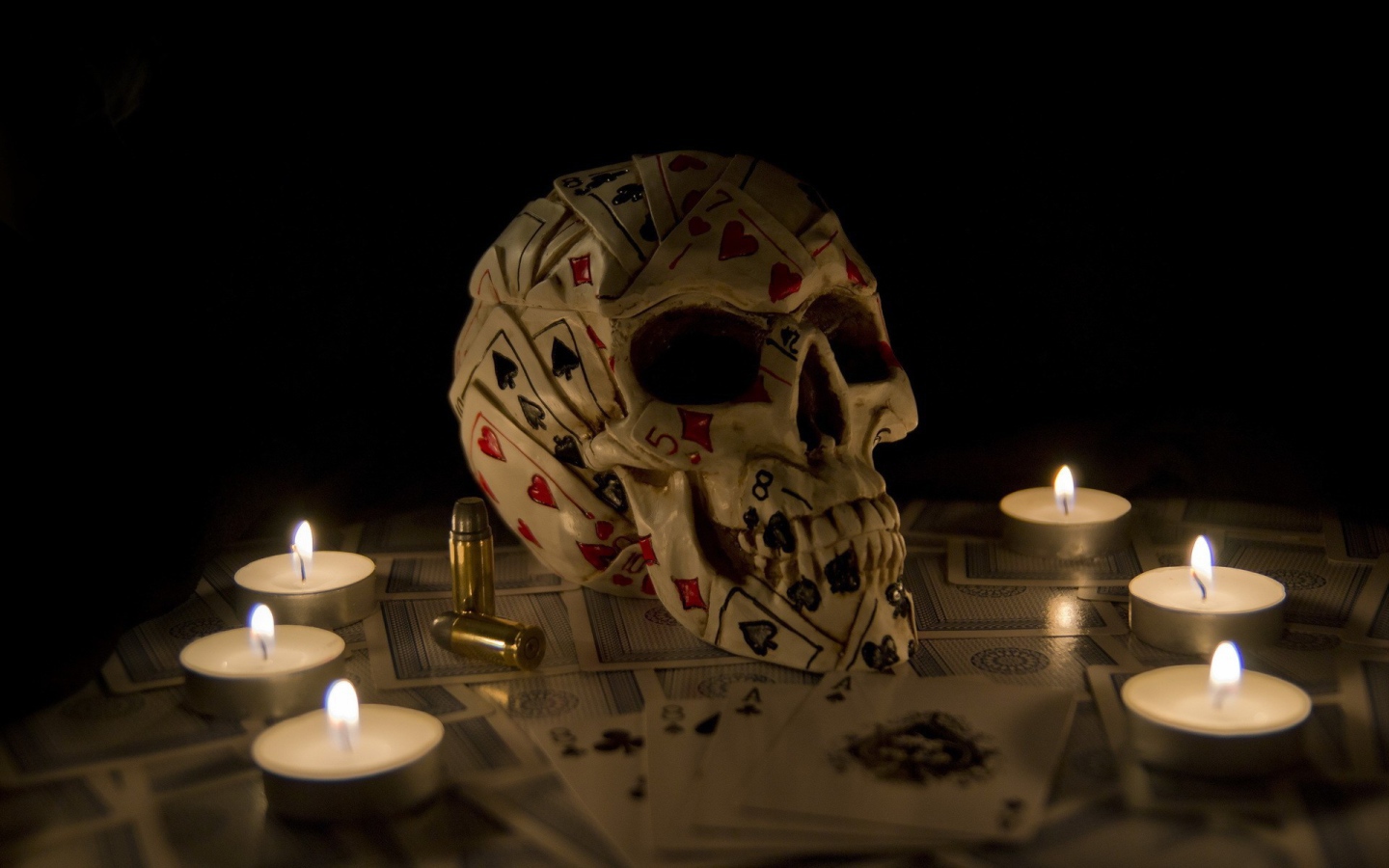 Череп из игровых карт среди свечей