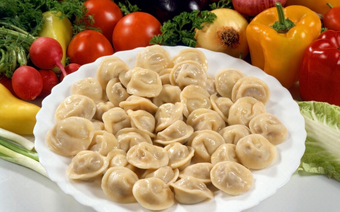 Пельмени на тарелке среди овощей