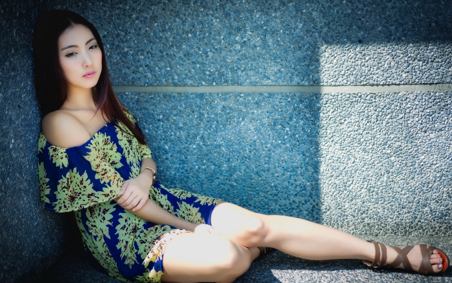 Девушка сидит в тени у гранитной стены