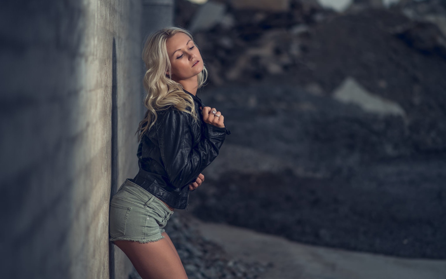 Блондинка в джинсовых шортах стоит у стены
