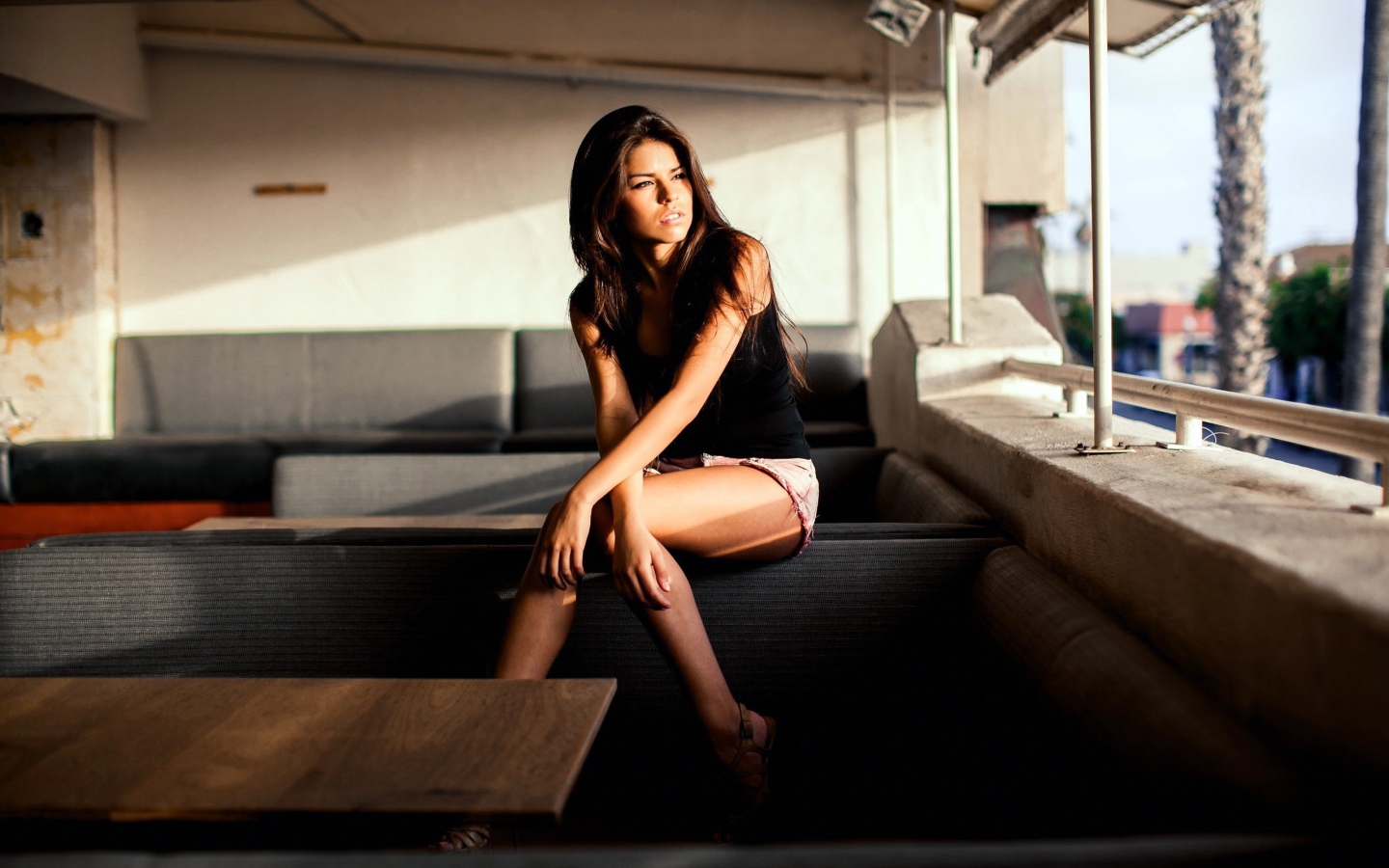 Брюнетка сидит на спинке дивана и смотрит в окно