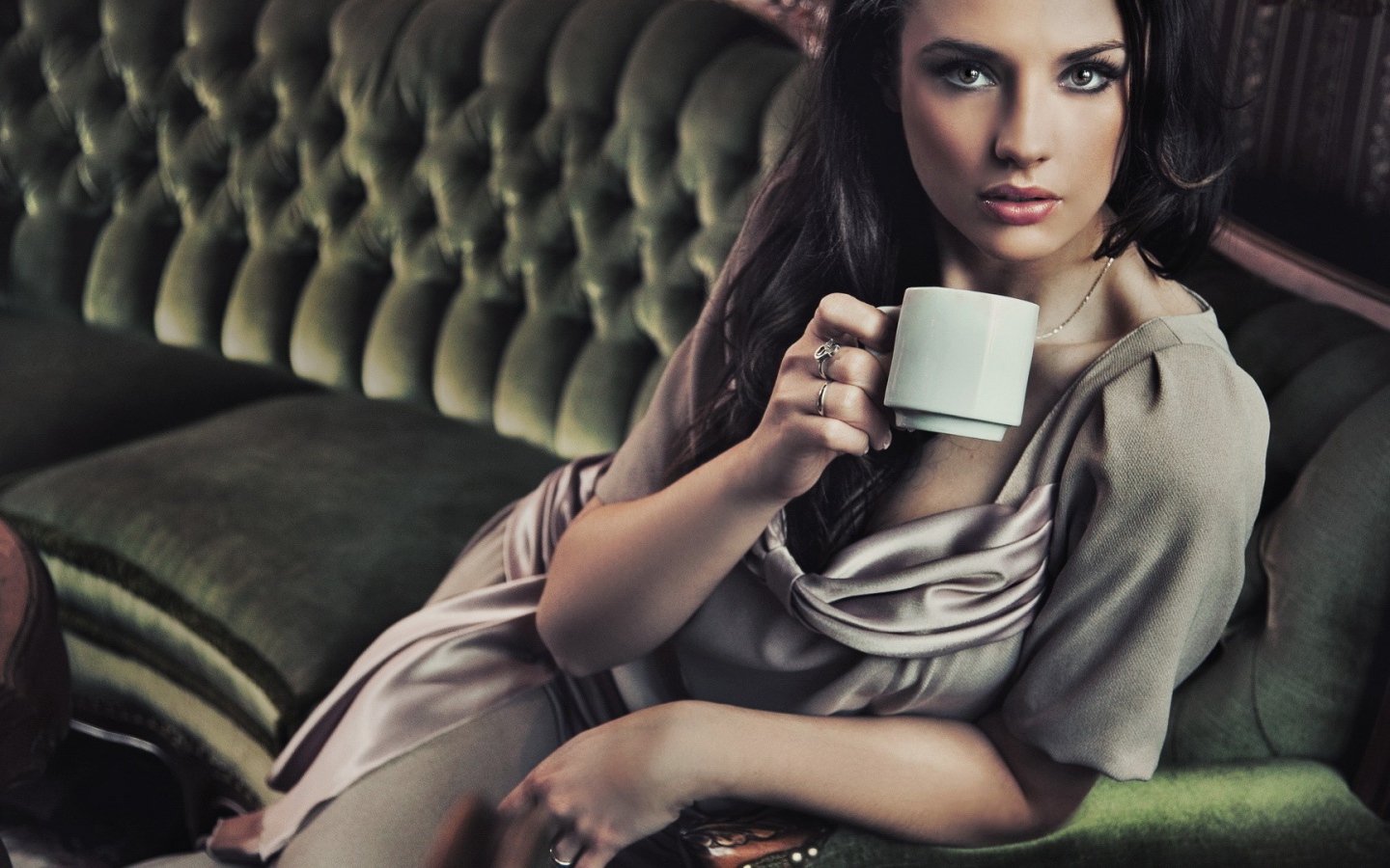 Брюнетка с чашкой кофе сидит на диване
