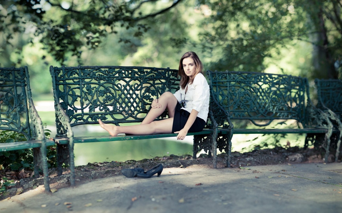 Девушка сидит на кованной парковой скамье