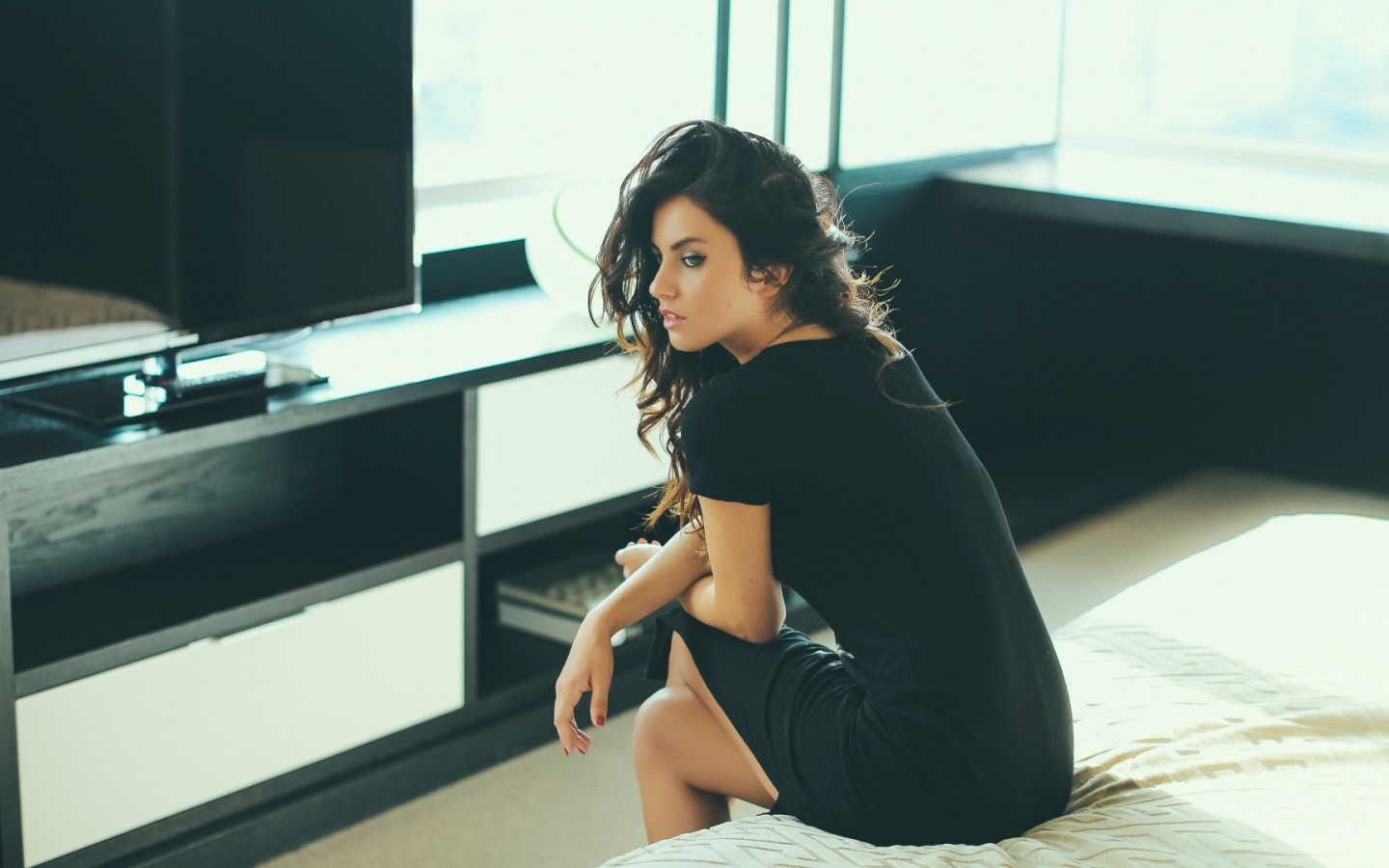 Девушка сидит на кровати перед телевизором