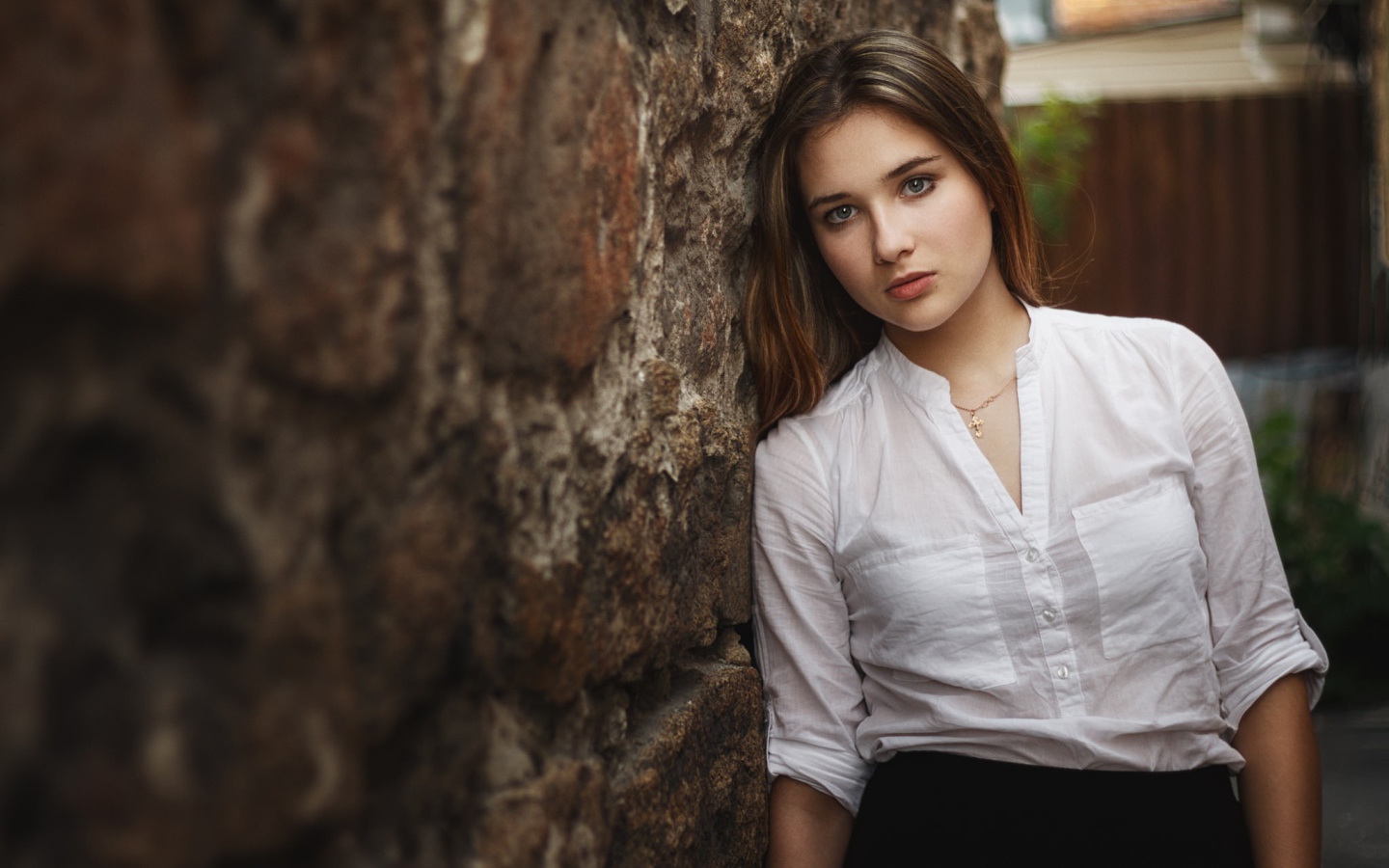Девушка в белой рубашке стоит у стены