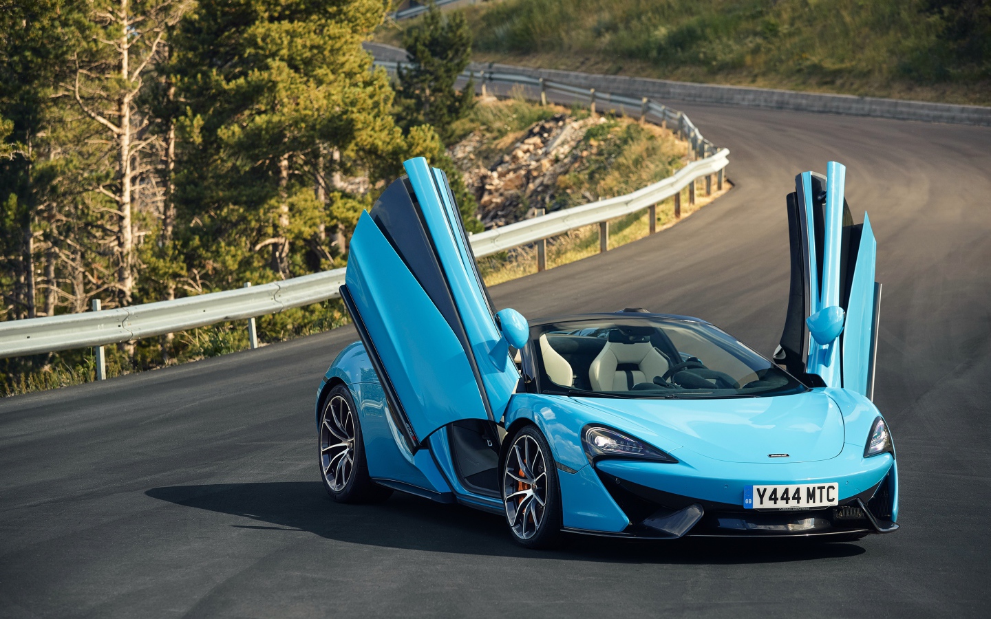 Синий спортивный автомобиль McLaren 570S на трассе с открытыми дверями