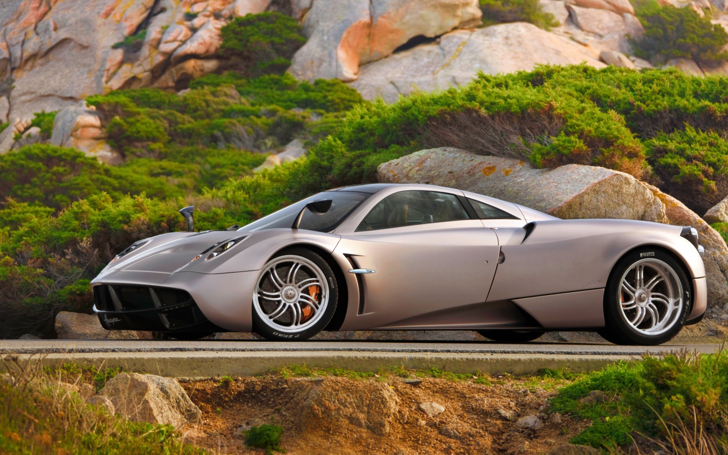 Серебристый быстрый автомобиль  Pagani Huayra на трассе у скалы