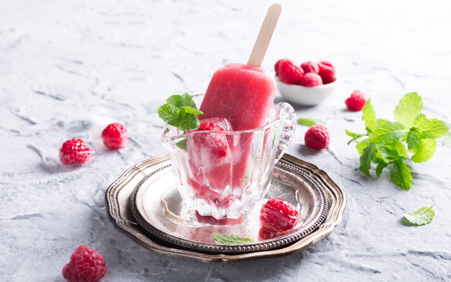 Малиновое мороженое на палочке в стеклянном стакане на столе со свежими ягодами