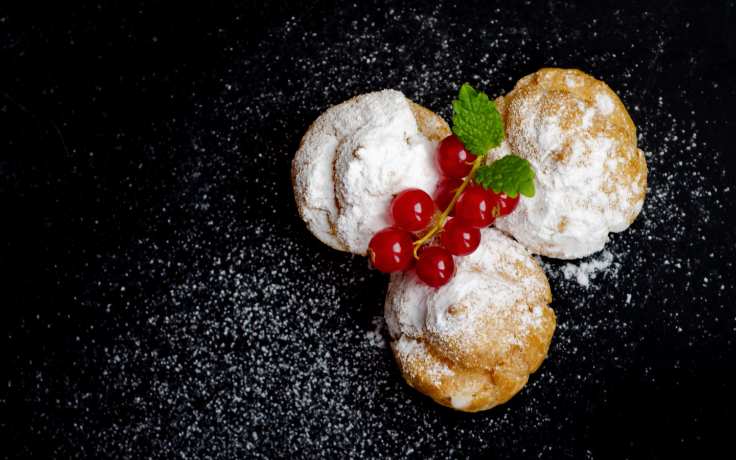 Три пирожных с сахарной пудрой и красной смородиной на черном фоне