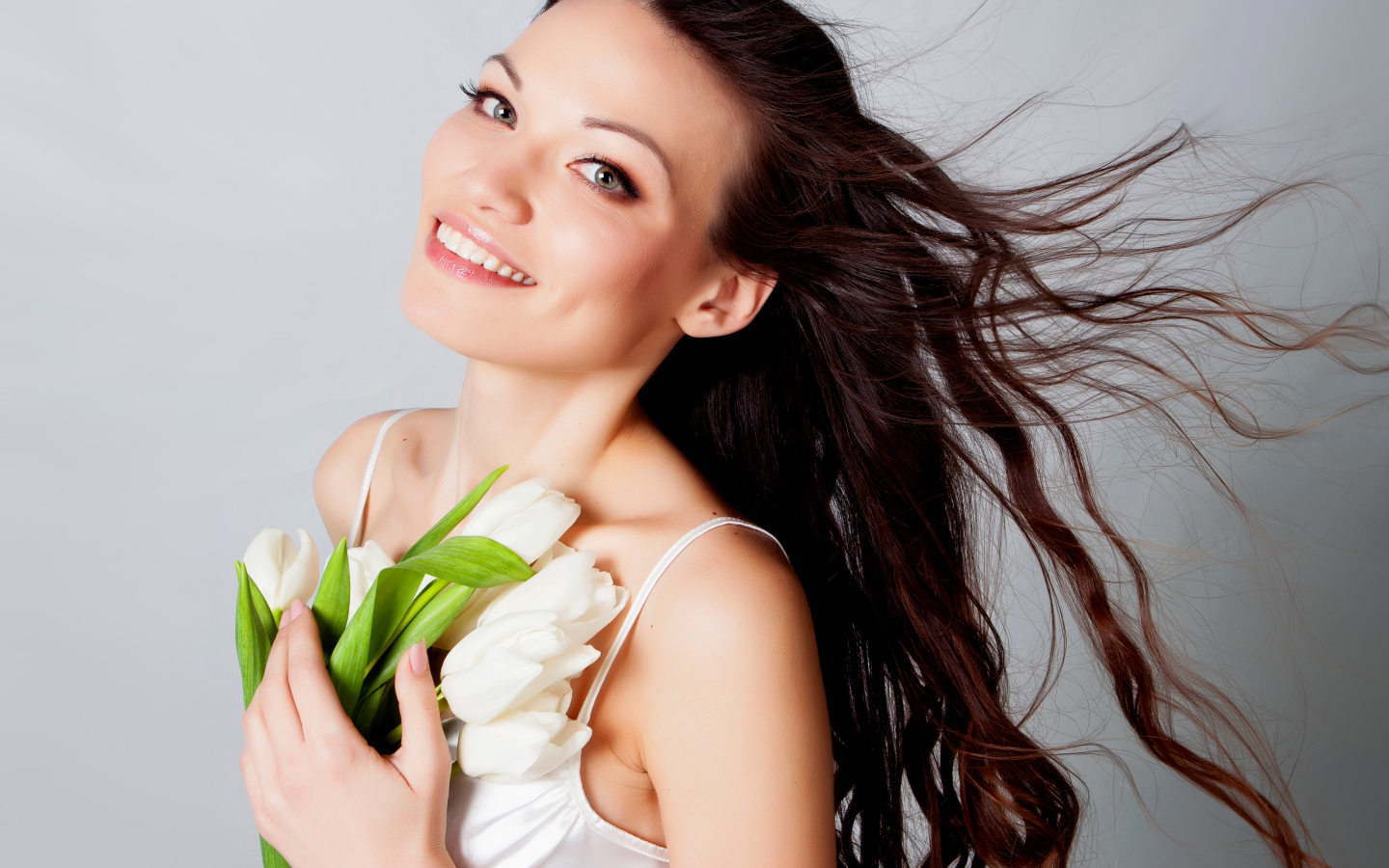 Красивая улыбающаяся брюнетка с букетом тюльпанов на сером фоне