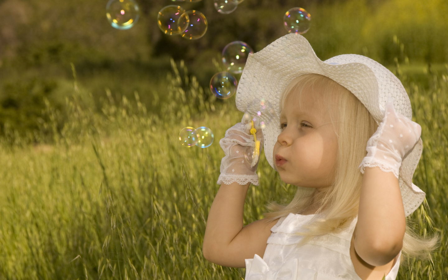 Маленькая девочка в большой белой шляпе пускает мыльные пузыри