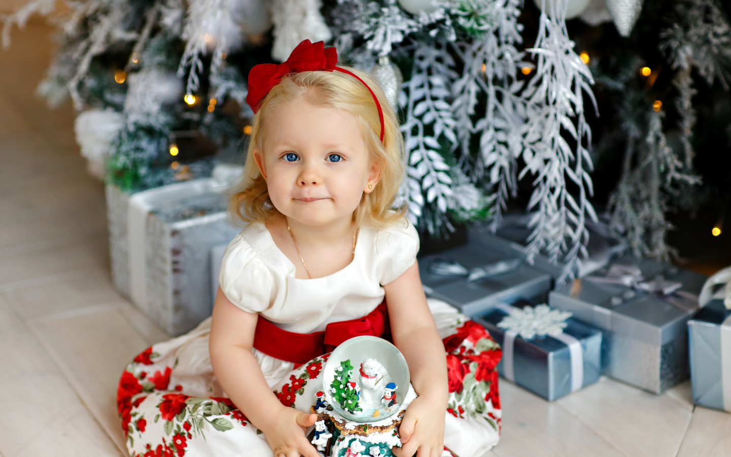 Маленькая девочка блондинка сидит с подарками под новогодней елкой