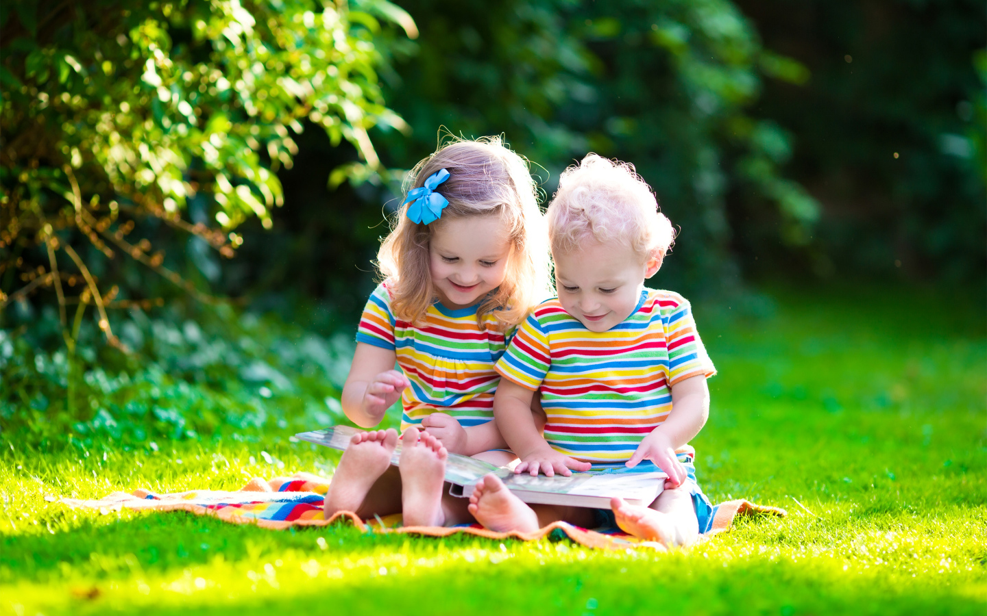 Маленькие мальчик и девочка читают книгу сидя на зеленой траве