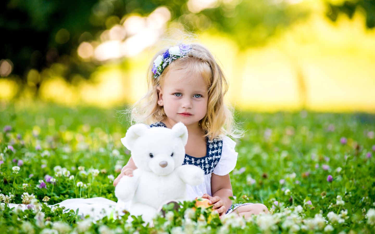 Маленькая милая девочка с игрушкой сидит на зеленой траве с цветами