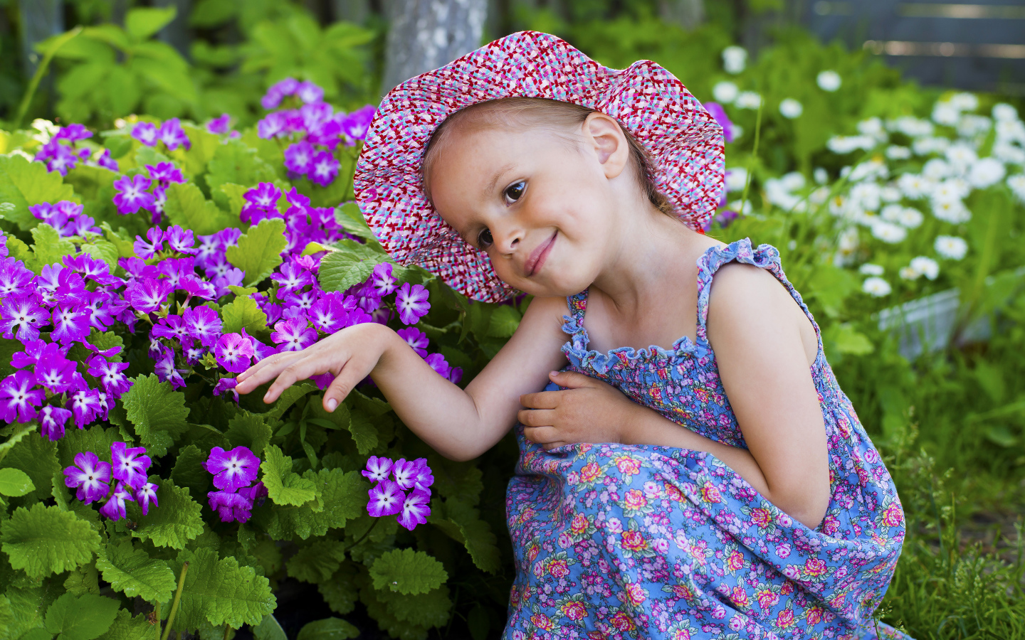 Маленькая девочка в шляпе рядом с фиолетовыми цветами