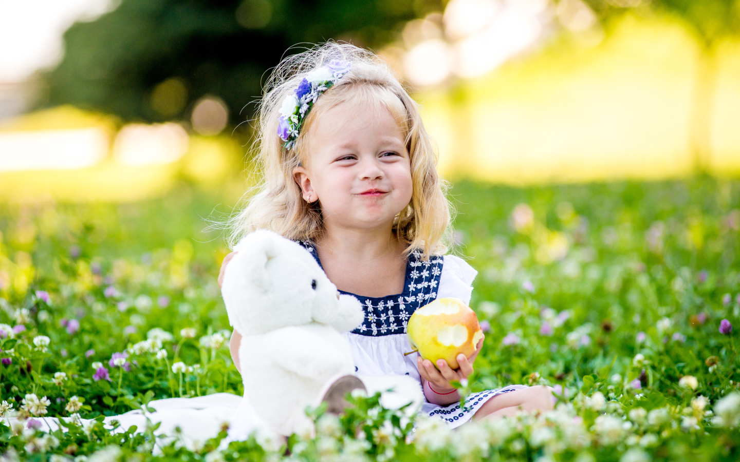 Маленькая девочка с белым медвежонком в руках и большим яблоком
