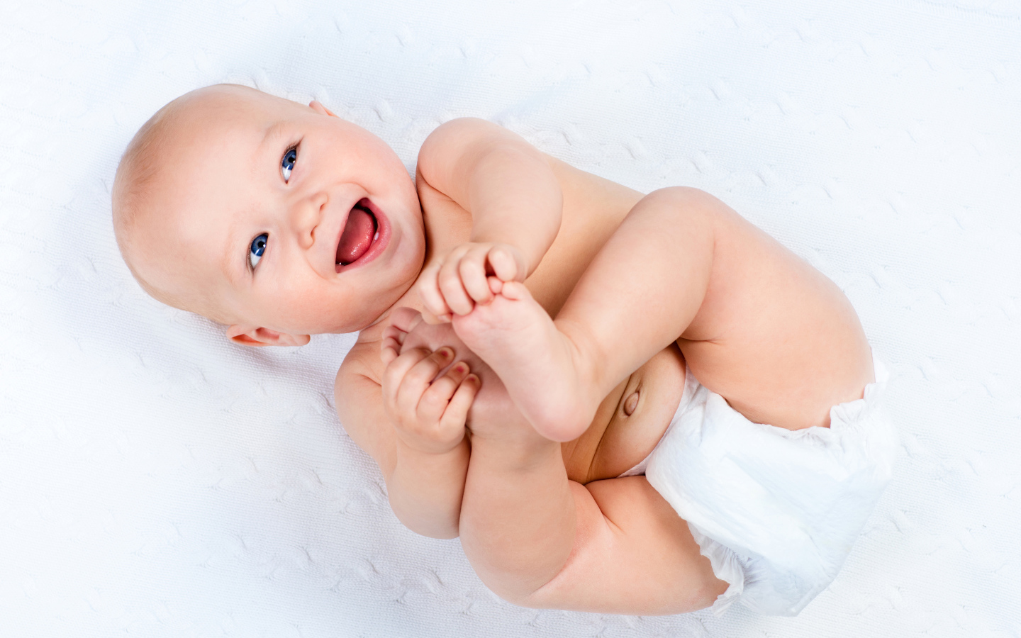 Маленький улыбающийся грудной ребенок держит руками ноги
