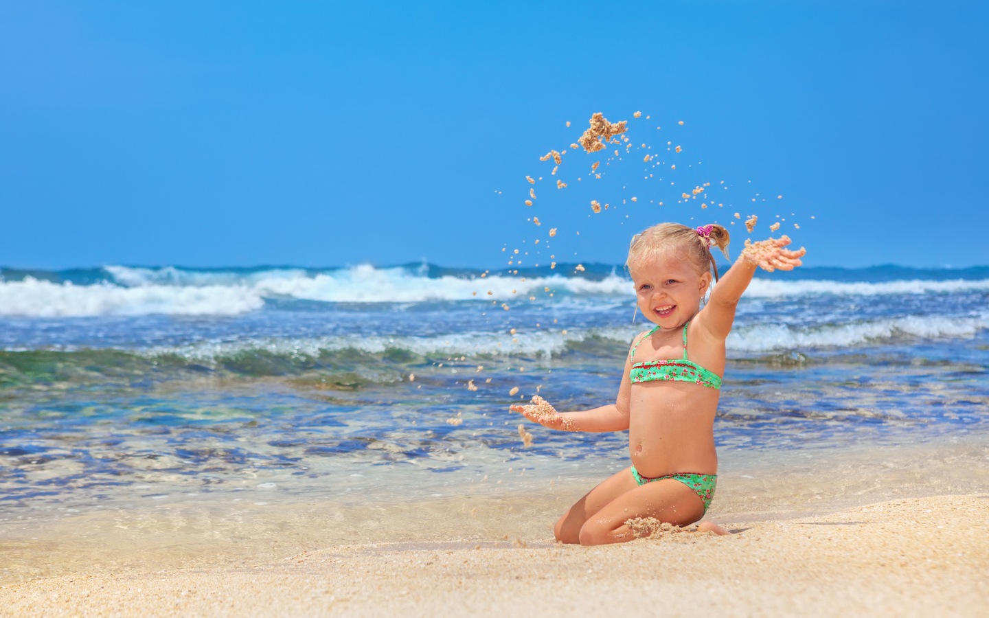 Маленькая улыбающаяся девочка играет на пляже с песком