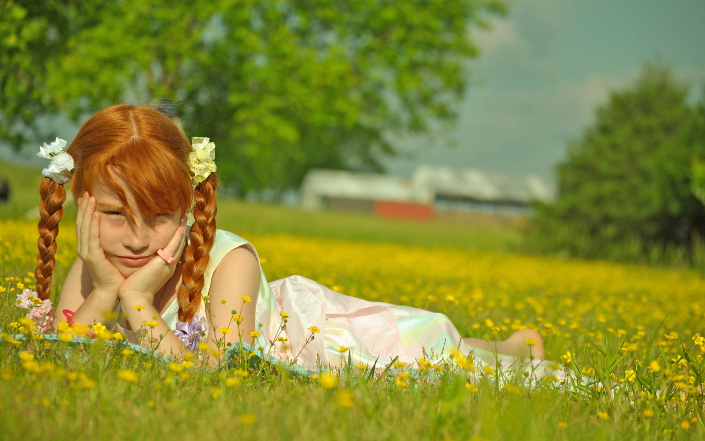 Рыжеволосая девочка с косичками лежит на зеленой траве