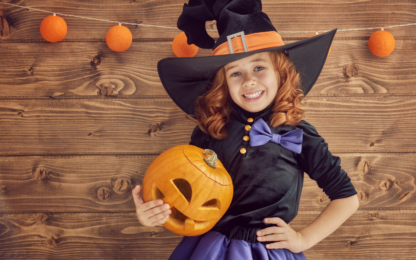 Улыбающаяся маленькая девочка в костюме ведьмы с тыквой на Хэллоуин