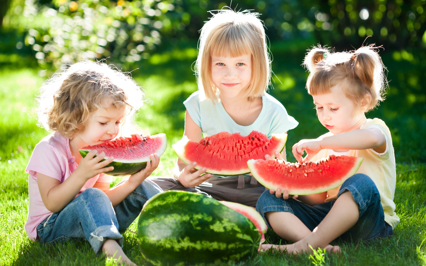 Три маленькие девочки едят арбуз на зеленой траве летом
