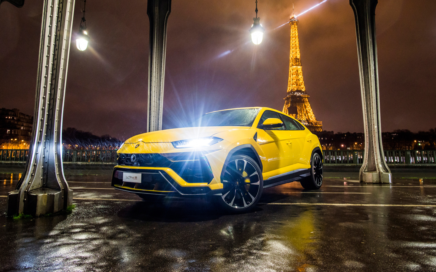 Желтый Lamborghini Urus, 2018 с включенными фарами на фоне Эйфелевой башни