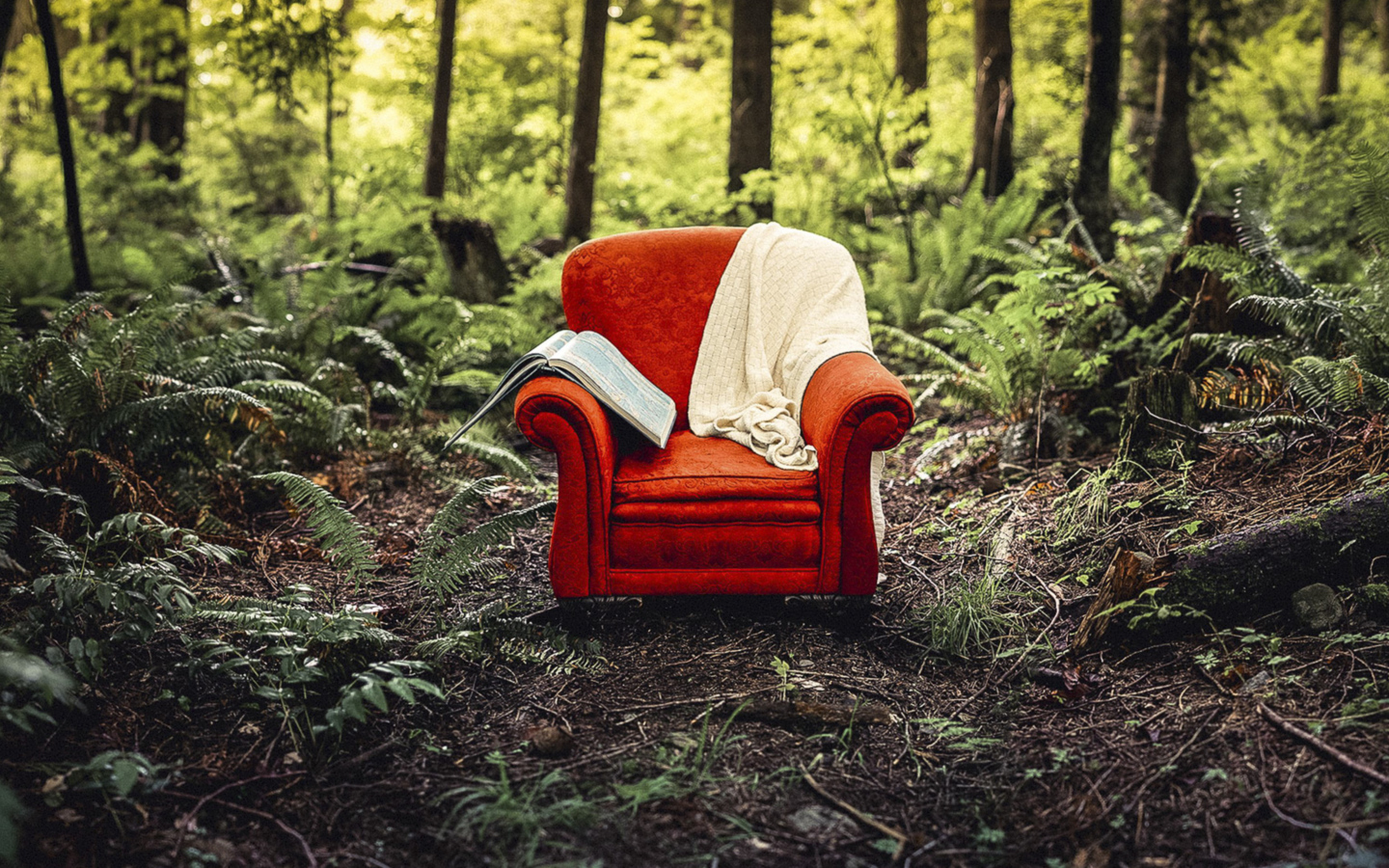 Старое красное кресло с книгой и пледом в лесу 