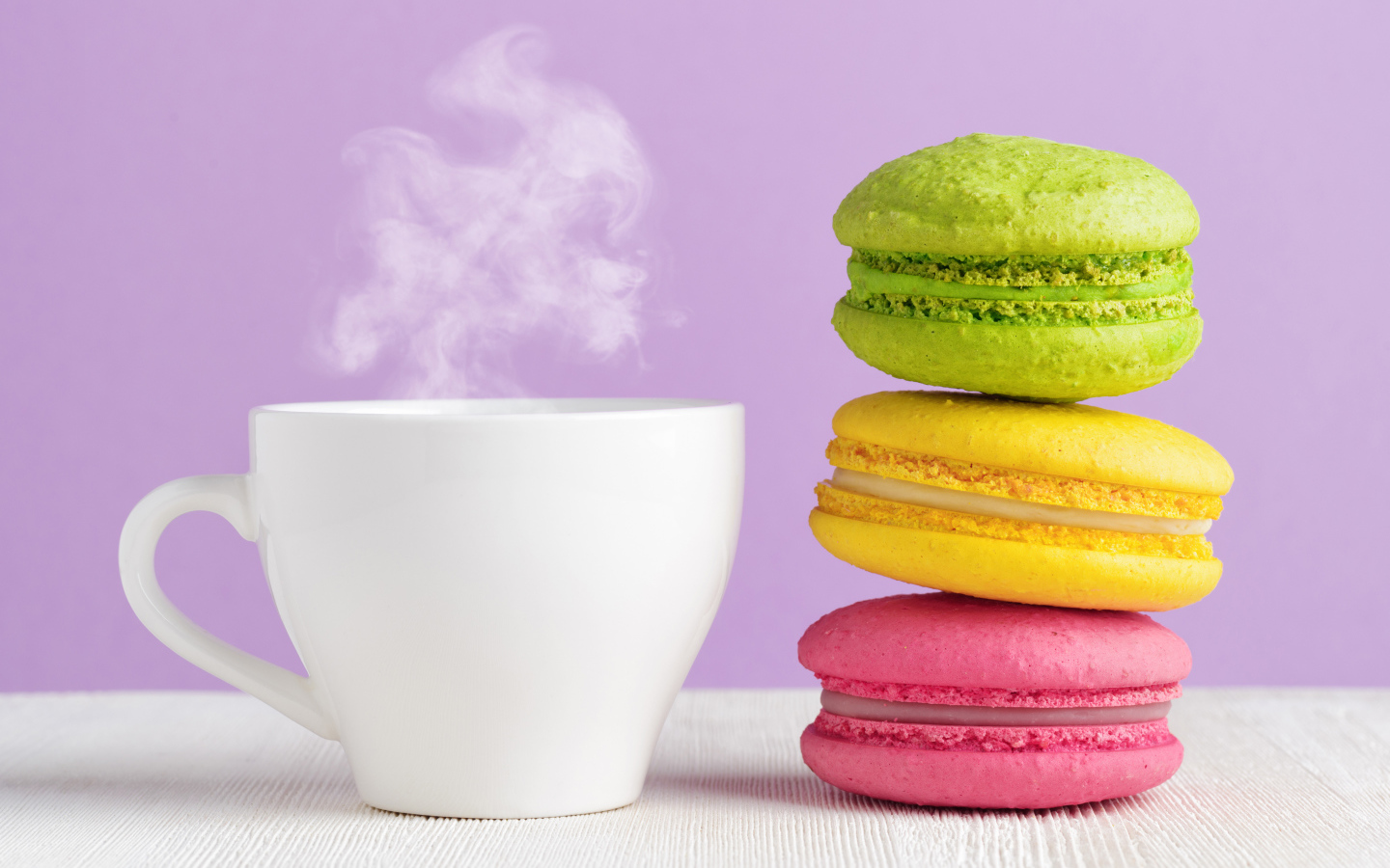 Разноцветный десерт макарун с чашкой горячего кофе на столе