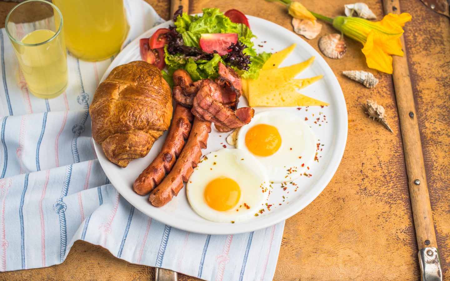 Яичница, салат, сосиски и круассан с соком на завтрак 