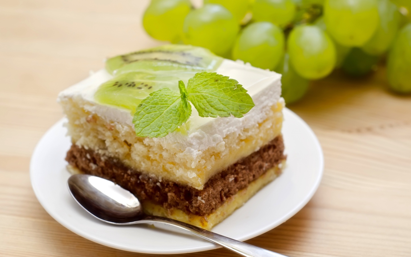 Кусок торта с киви и мятой на столе с виноградом