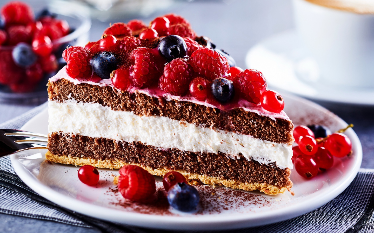 Аппетитный кусок торта на тарелке с ягодами малины, красной смородины и черники