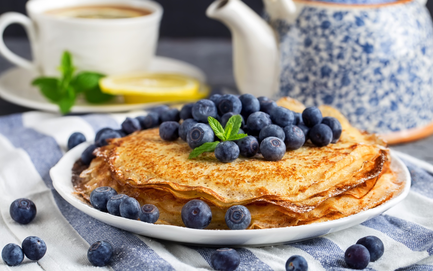 Тонкие блины с ягодами черники на столе с чаем